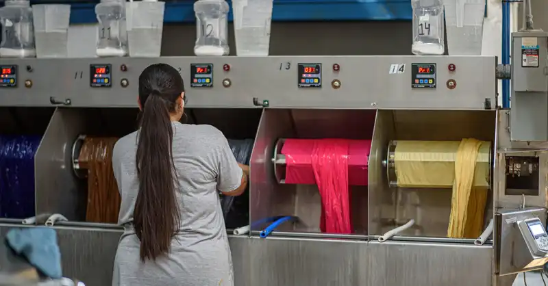 Person operating machines where fabrics are being dyed purple, brown, grey, pink, and yellow