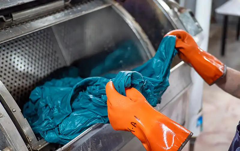 Person wearing orange gloves holding a turquoise colored garment being dyed in a machine